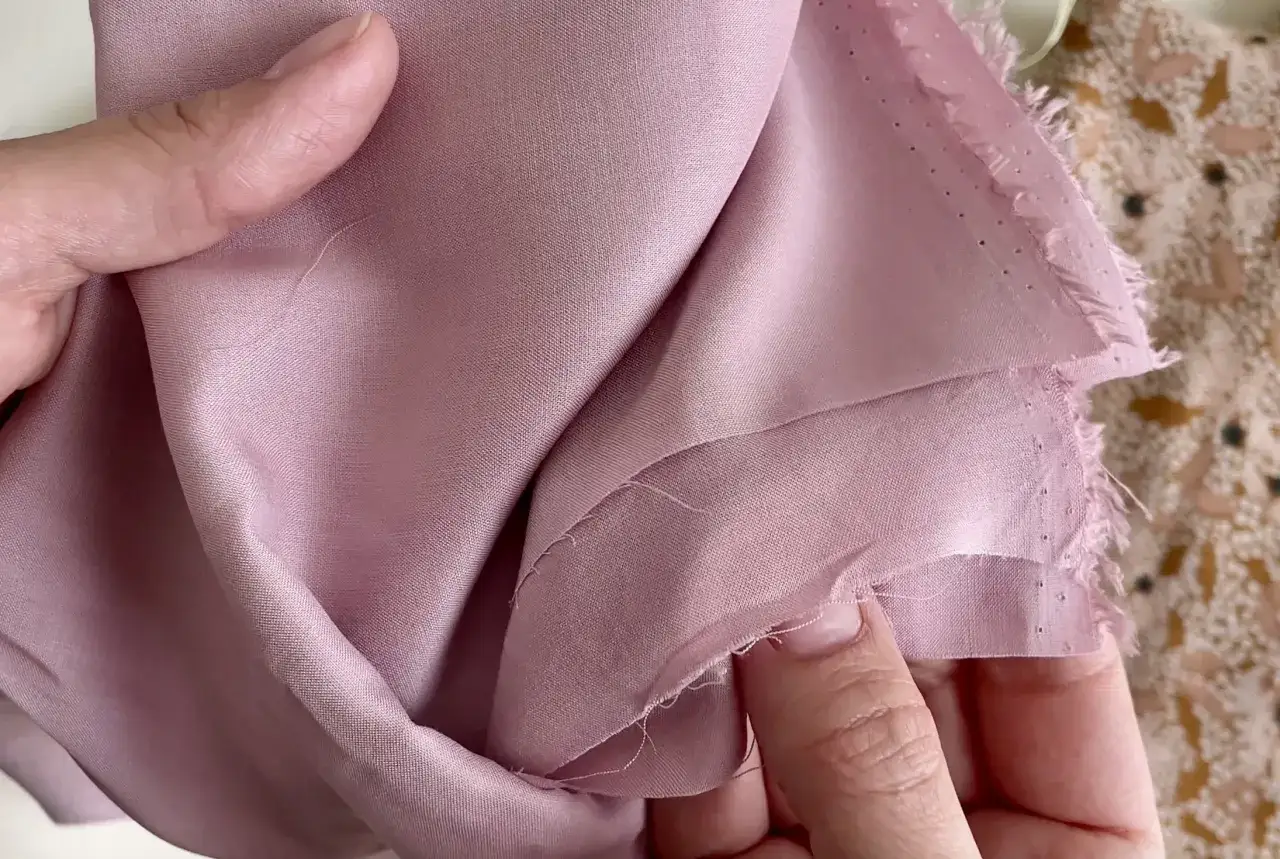 Mani che accarezzano un tessuto di viscosa rosa cipria, mostrando come lavare la viscosa a mano per preservarne la morbidezza.