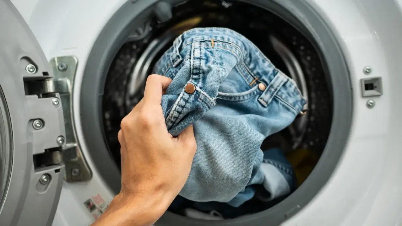 Mano inserisce jeans nella lavatrice, scopri come evitare che i jeans perdano colore.