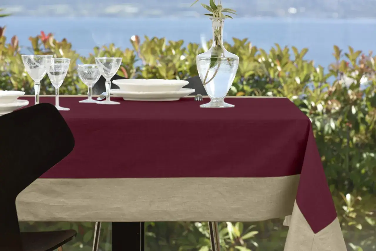 Tovaglia di lino bordeaux con bordo beige, apparecchiata per un pasto all'aperto. Un esempio di come rifinire una tovaglia di lino con stile.