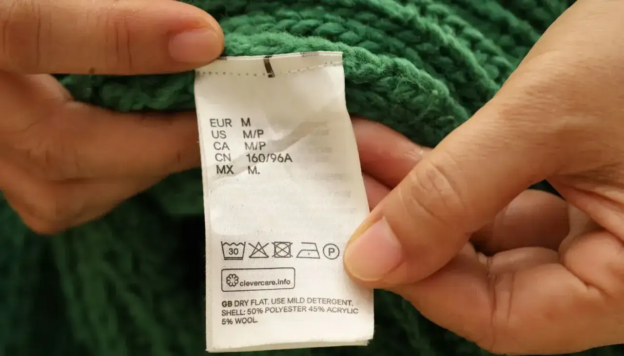 Etichetta di un maglione verde: lavare a 30 gradi, non candeggiare, non asciugare in asciugatrice, stirare a bassa temperatura, lavaggio a secco consentito.