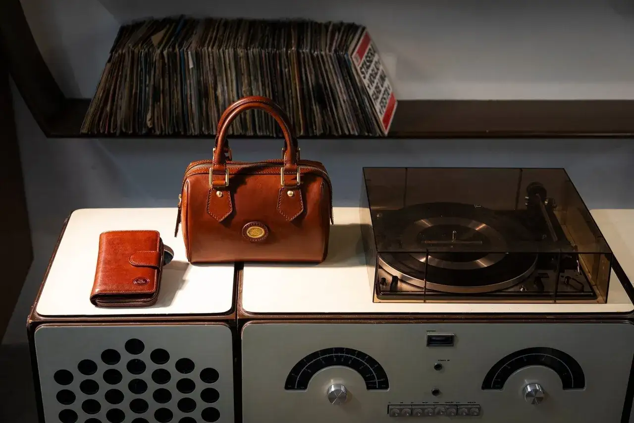 Borsa in pelle marrone e portafoglio, pronti per essere puliti, accanto a un giradischi vintage e dischi in vinile.
