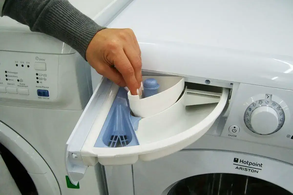 Mano inserisce un tappo nel cassetto della lavatrice, pronto per aggiungere candeggina.