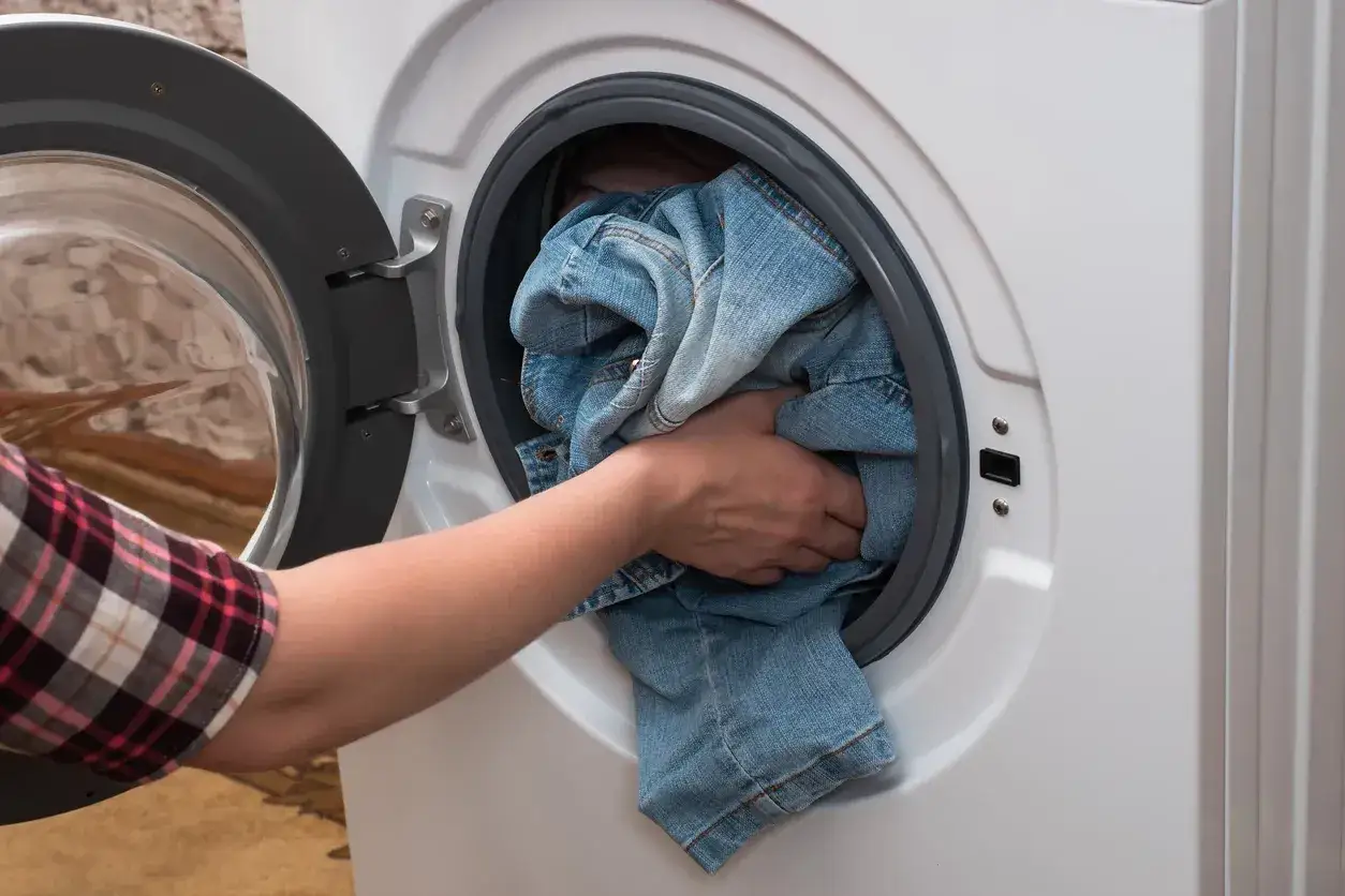 Mano inserisce un carico di jeans nella lavatrice per un ciclo di denim.