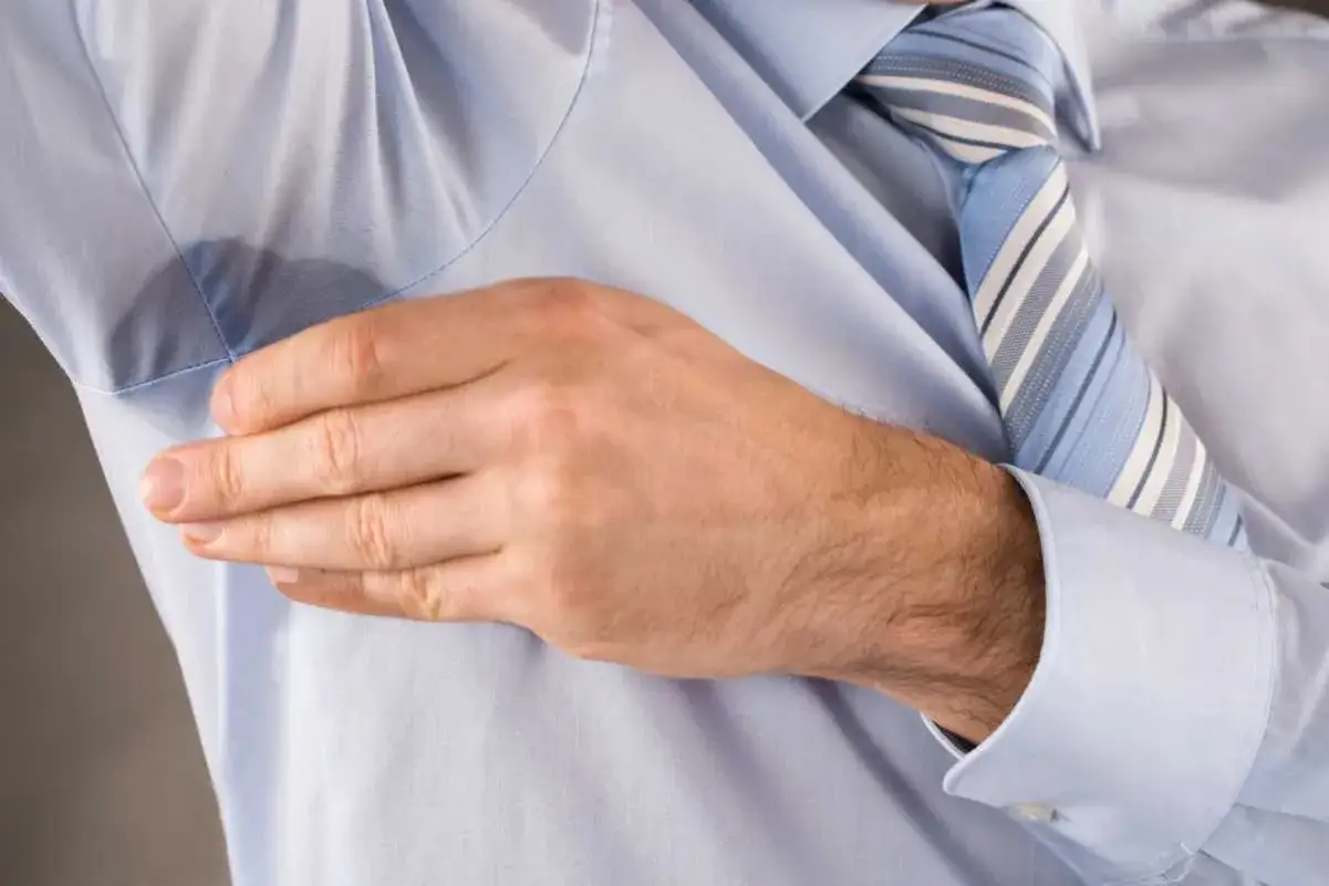 Uomo con camicia azzurra e cravatta a righe, mano sotto l'ascella per mostrare le macchie di sudore vecchie.