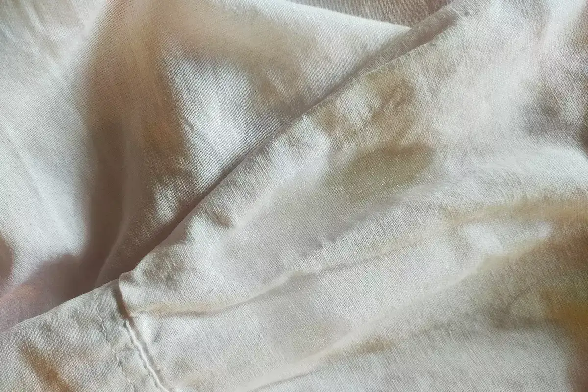 Tessuto di lino chiaro con macchie evidenti, un esempio pratico per capire come smacchiare il lino e riportarlo al suo splendore originale.