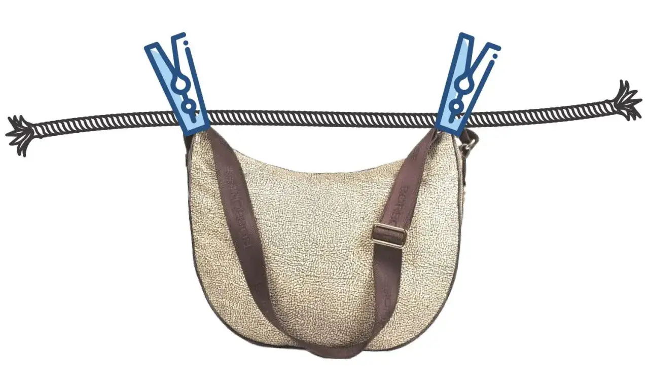 Come lavare una borsa di tela e pelle: la borsa &egrave; appesa ad asciugare con mollette su un filo.