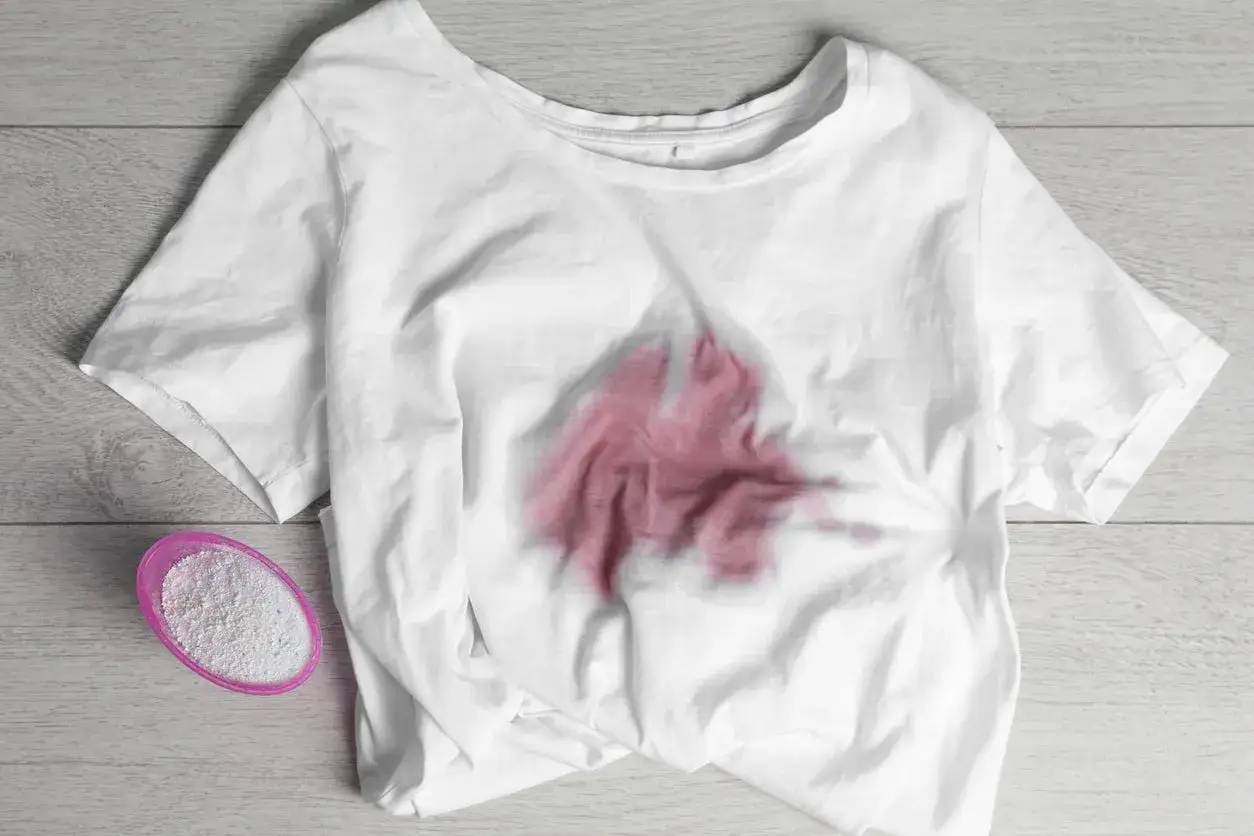 Camicia bianca macchiata di rosa, con un misurino di detersivo. Come sbiancare una camicia bianca diventata rosa?