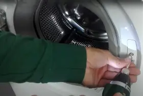 Mano con avvitatore che lavora sul pannello di una lavatrice che non esegue i programmi.