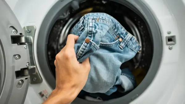 Mano inserisce jeans nella lavatrice. Scopri come lavare i jeans in lavatrice per mantenerli come nuovi.