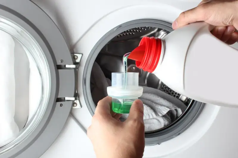 Versando detersivo liquido in un misurino per lavatrice. Ideale per capi delicati, cosa lavare a 20 gradi per preservare i colori.